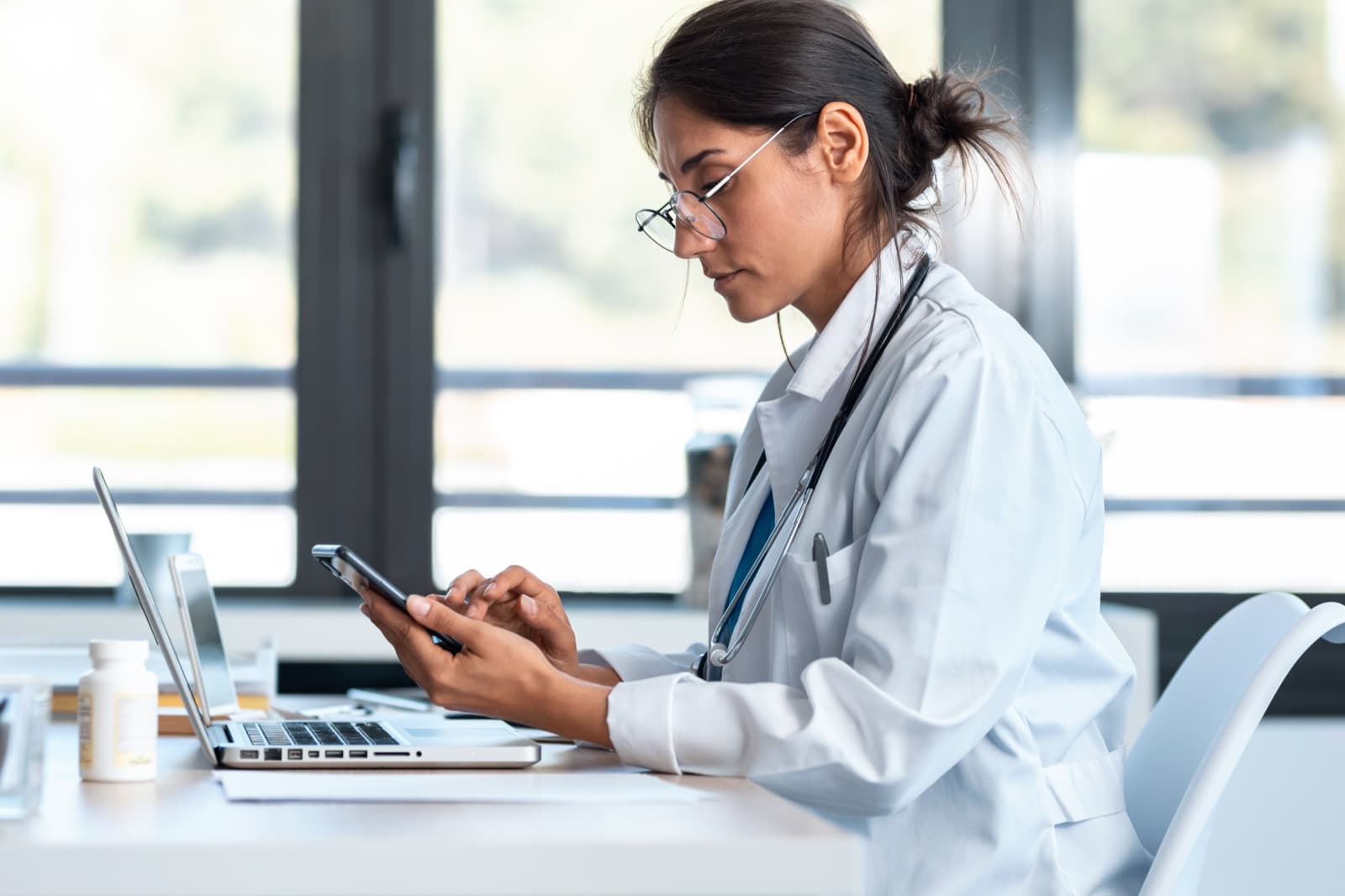 Médica consultando o celular enquanto trabalha no consultório